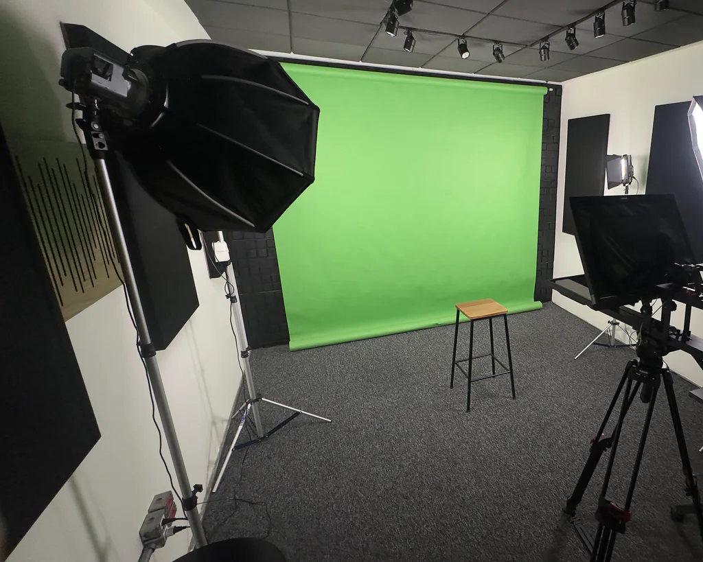Estúdio com fundo chroma key verde, banco de madeira, tripé de câmera e painéis de isolamento acústico na Capto