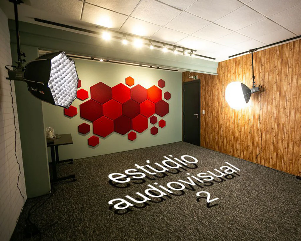Estúdio audiovisual 2 da Capto com painel de acústica hexagonal vermelho, parede de bambu e softbox de iluminação