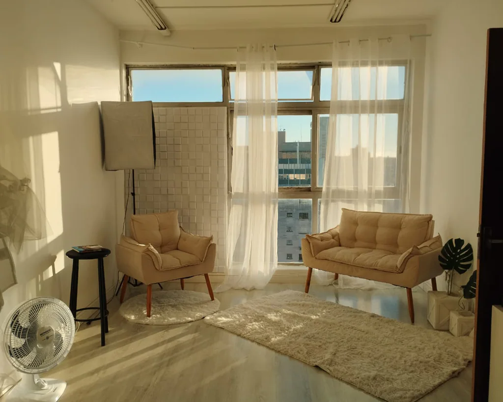 Dois ambientes de cenário com poltronas bege, softbox de iluminação e vista da cidade no Estúdio Grimm