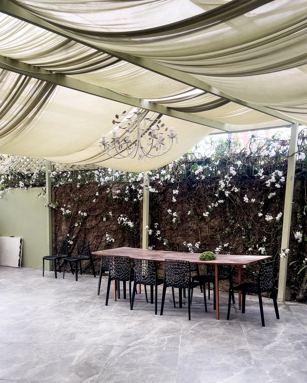 Quintal coberto com tecido drapeado, lustre e parede florida no Espaço Iluminar Café, Amor e Cura