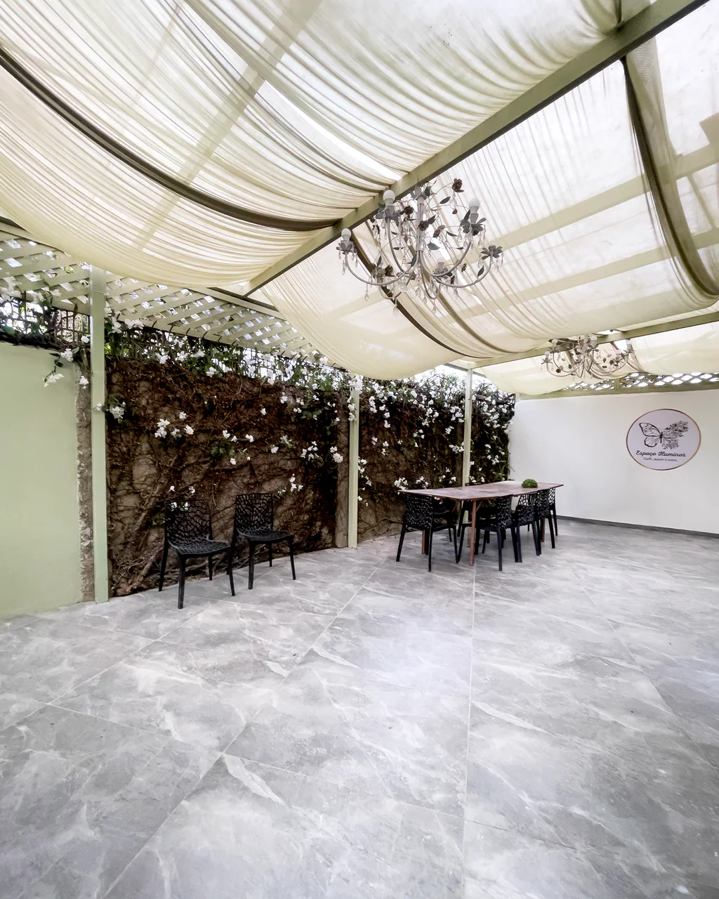 Quintal coberto com mesa longa para eventos e logo do Espaço Iluminar na parede