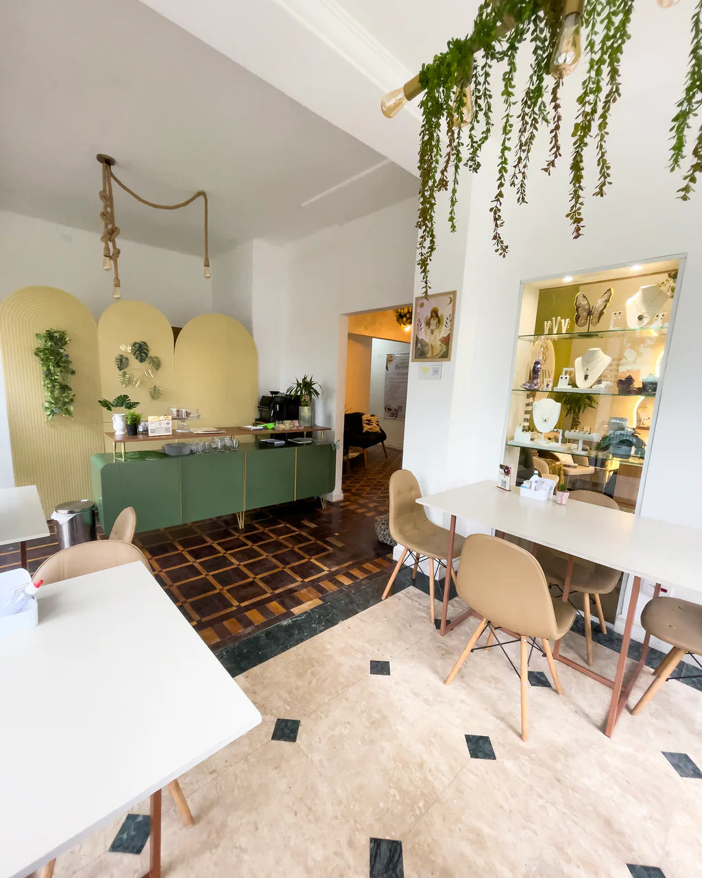 Balcão do café com arcos amarelos, plantas suspensas e vitrine de joias no Espaço Iluminar