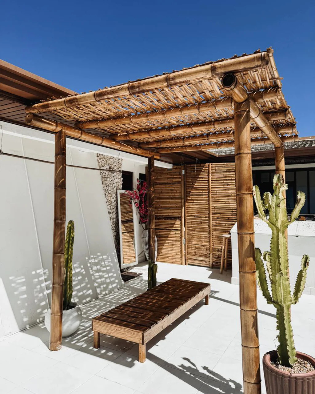 Terraço com pergolado de bambu, banco de madeira e cactos no Studio Jardim Secreto