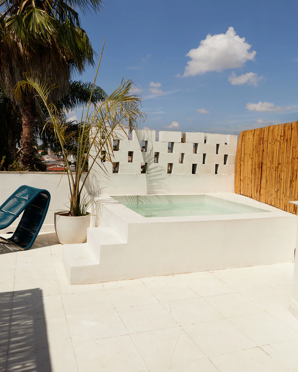 Piscina no terraço com palmeiras, cadeira azul e painel de bambu no Studio Jardim Secreto