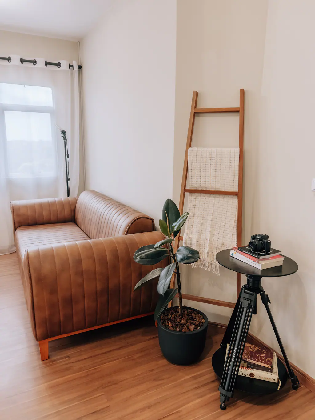 Sofá de couro caramelo, planta, escada decorativa de madeira e tripé com câmera no Macchiato