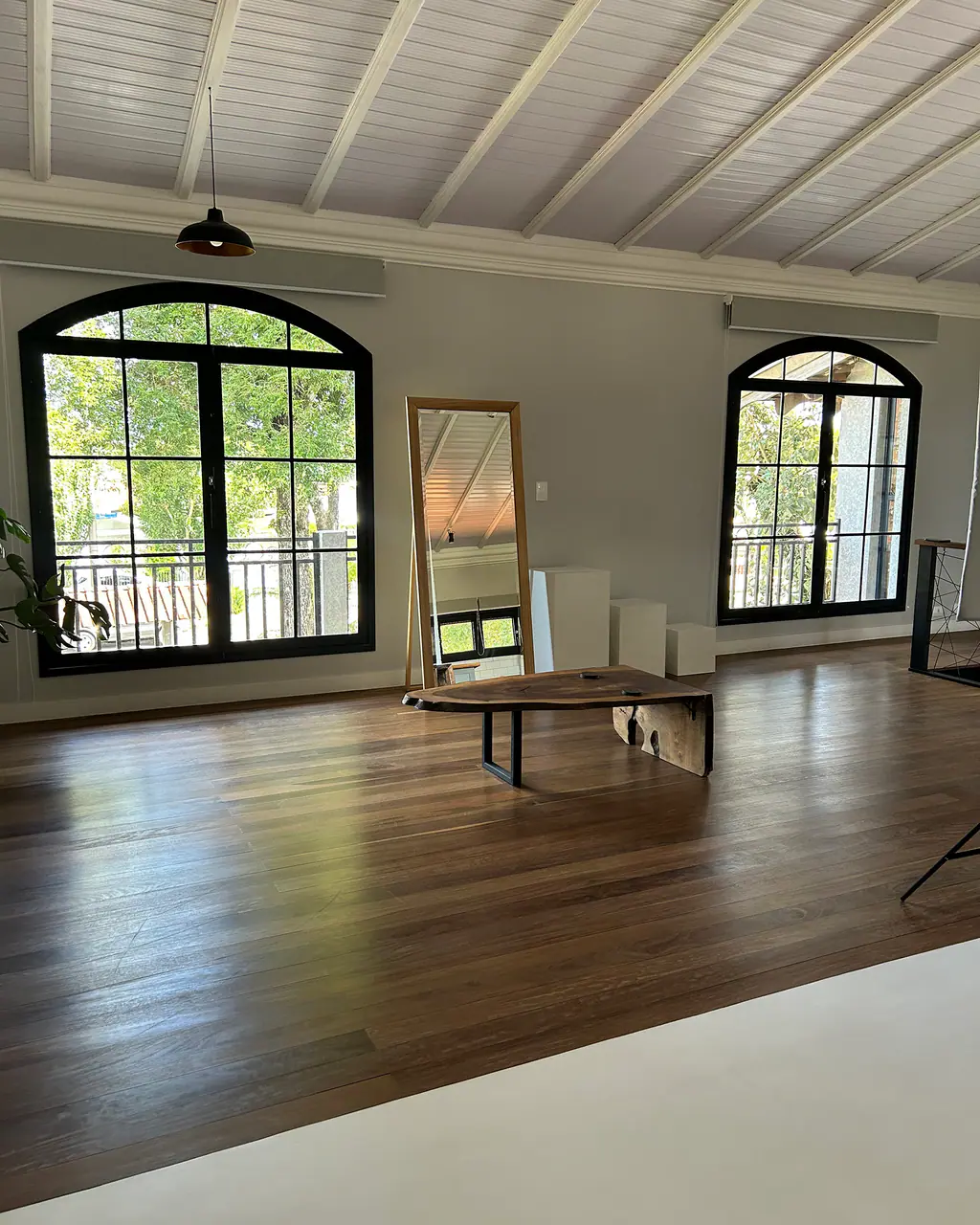 Sala ampla com espelho de corpo inteiro, mesa de centro de madeira e janelas arqueadas em ferro no Mammü estúdio