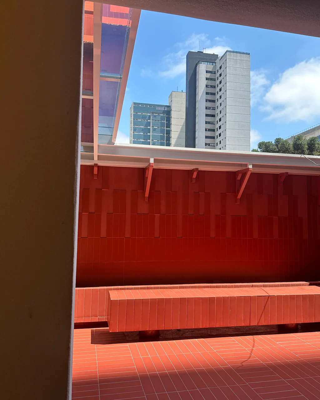 Área externa do ONCÈ Studio vista por um vão circular, com mesa oval, cadeiras e parede revestida em tons terracota