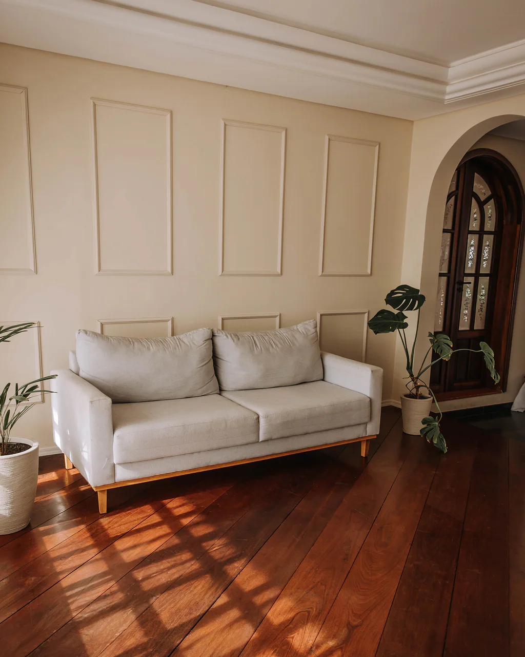 Sala com sofá claro, plantas e luz do sol sobre o piso de madeira no Studio Keeper